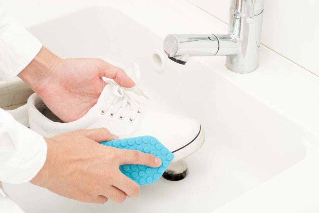 someone washing off some white sneakers over a sink