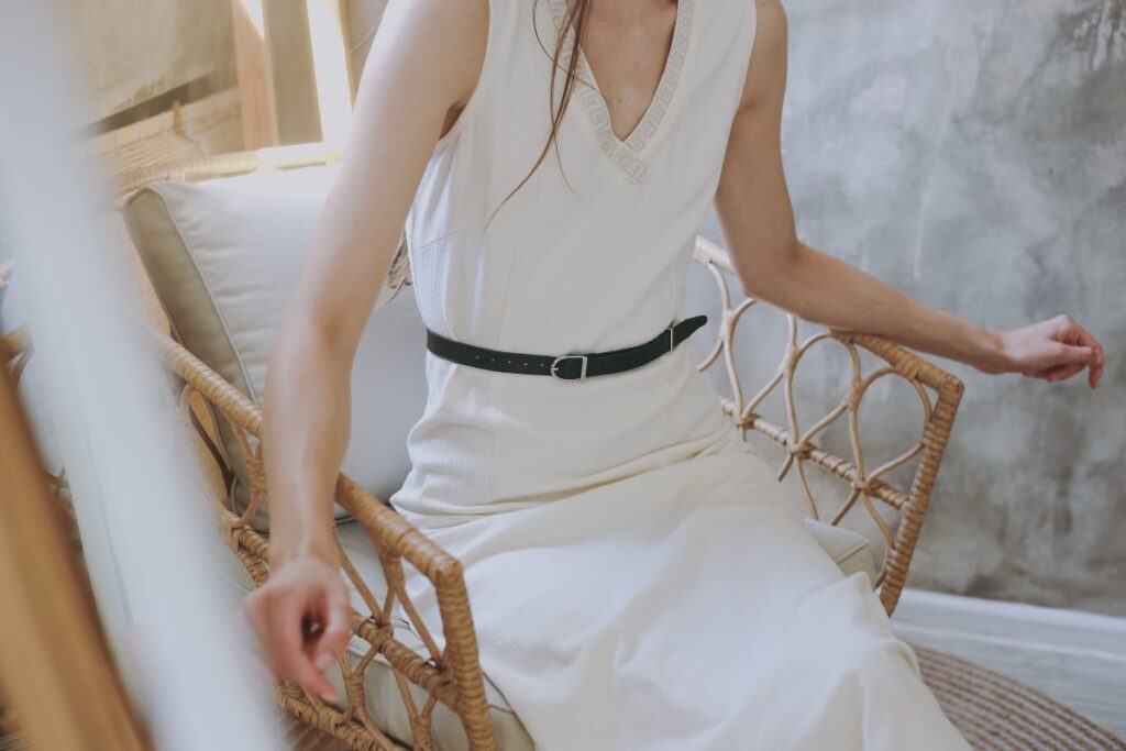 a woman sitting down in a white dress with a black belt